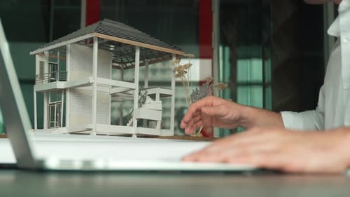 Architect Works on Laptop with House Model