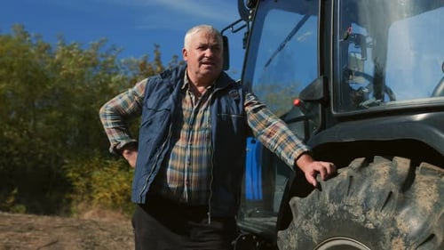 Farmer Stands Next to Tractor on a Sunny Day