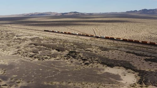 Ein extrem langer Güterzug mit vielen Waggons rast eine Bahnstrecke hinunter durch eine Wüstenlandschaft