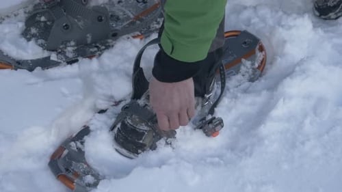 Senior man fastening snowshoes in snowy winter preparation for travel