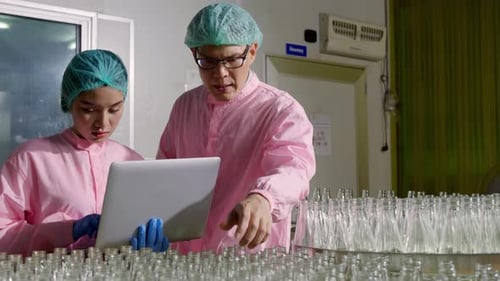 Deux ingénieurs supervisent le contrôle qualité en vérifiant les bouteilles de produits sur le tapis roulant d'une usine de boissons