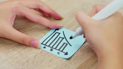 Close-up of Hand drawing downward trend arrow on bar chart sticky note