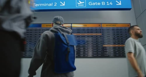 Airport Terminal Passengers with Luggage and Tickets Checking Departures on Digital Departure Board