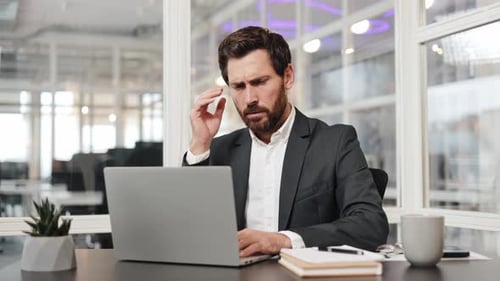 Businessman with Headache at Work on Laptop in Modern Office