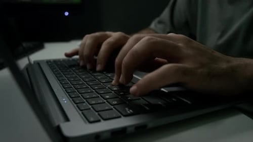 Nahaufnahme eines nicht wiederzuerkennenden Mannes, der schnell auf der Laptoptastatur am Schreibtisch tippt