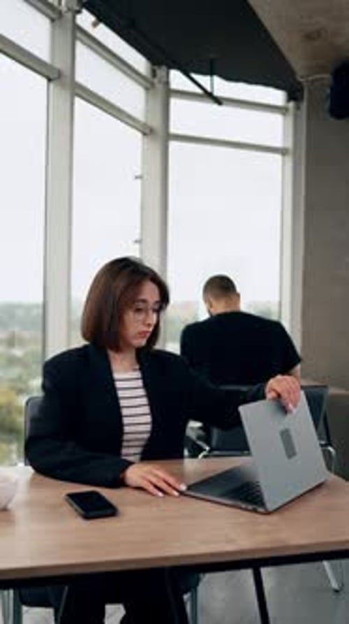 Brunette woman sitting at desk opens her laptop. Business lady starts work on laptop.