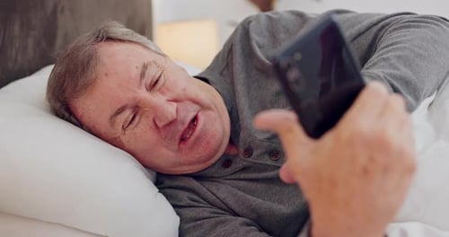 Man Lying in Bed Laughing at Smartphone
