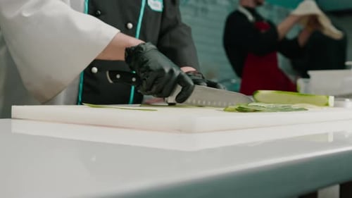 Close-up of a sushi maker in gloves cutting a cucumber with a professional kitchen knife