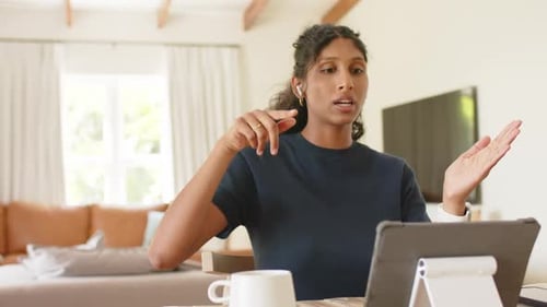 Femme afro-américaine répondant à une invite de tablette, pointant du doigt et expliquant à la table de la maison avec une tasse