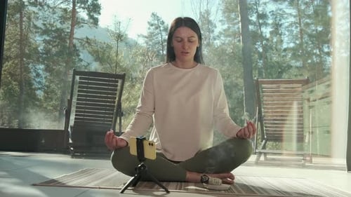 Woman Practicing Yoga and Meditation with Incense in Front of Smartphone