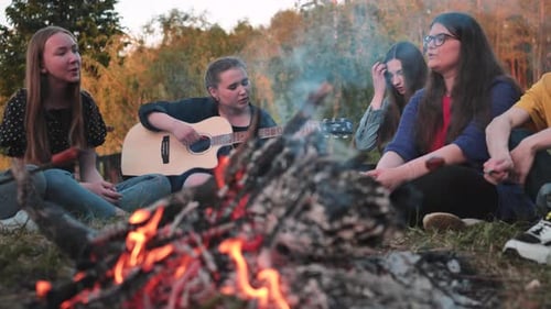 Young Adults Singing Around Campfire at Golden Hour