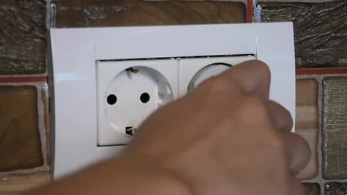 Close-up of the European wall power socket being plugged and unplugged by a woman hand.