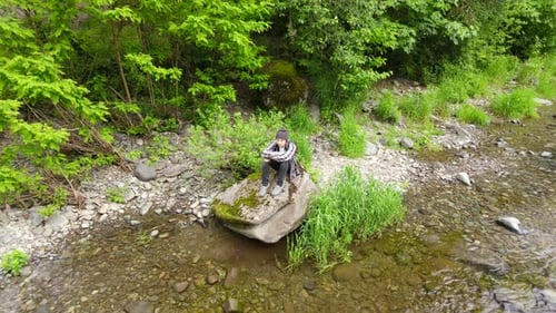 Person, die auf einem Felsen sitzt, während die Drohne wegfliegt und die Umgebung des Washougal River enthüllt und