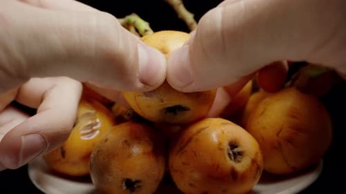 Des mains masculines sortent un loquat d'un bol et le déchirent en deux, le jus gicle et les graines tombent lentement