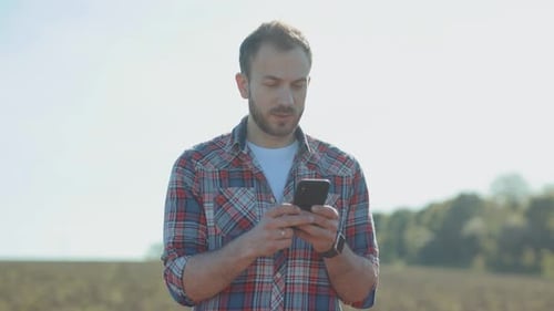 Man Using Smartphone in Rural Field on Sunny Day