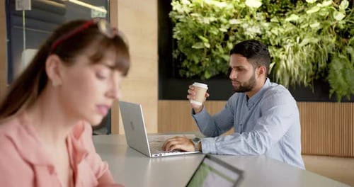 Travaillant au bureau, homme utilisant un ordinateur portable et tenant une tasse à café, femme utilisant une tablette