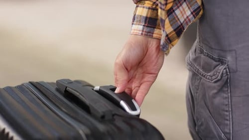 Mão direita pressionando o botão na mala na entrada do terminal, estendendo a alça telescópica para puxar