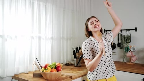 Cheerful Woman Dancing in Kitchen with Wooden Spoon