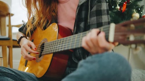 Playing Guitar By the Christmas Tree on a Cozy Winter Afternoon with Warm Lights and Festive