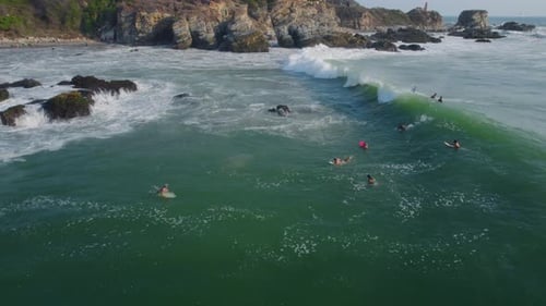 Surfers surfing next to rocks, over Rough sea with waves, Close Aerial shot.