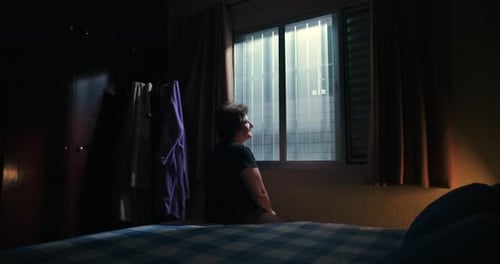 Woman Sits on Bed, Looking Out Window