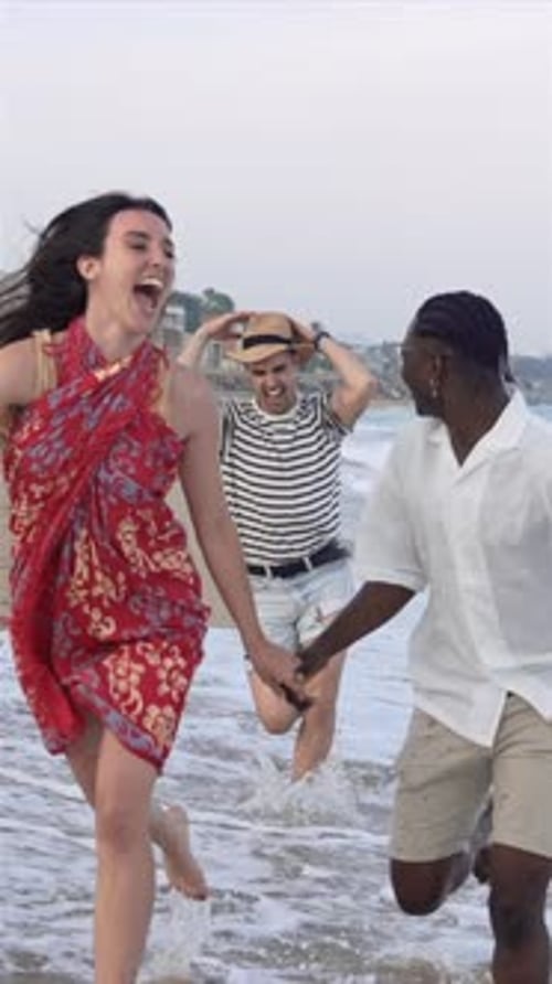 Happy Friends Barefoot Running Together Along the Beach at Sunset Splashing in the Water Waves