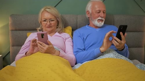Senior Couple Using Smartphones in Bed