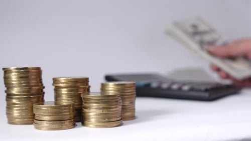 Gold Coins Stacked While Person Uses Calculator
