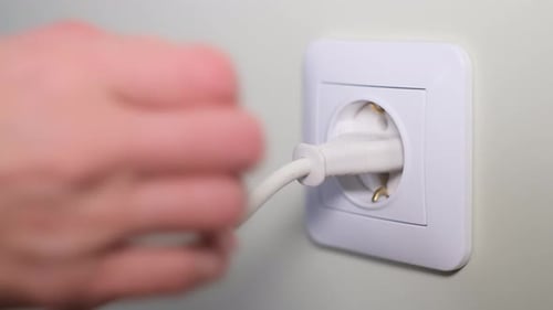Closeup of a Woman's Hand Pulling Out a Plug From an Electrical Outlet on the Wall