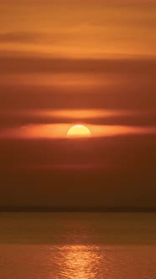 Vertical time lapse video of dramatic sunset over a lake in a cloudy day.