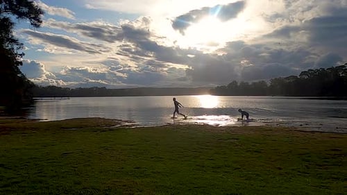 Children playing and running at the edge of a lake at sunset, dawn
