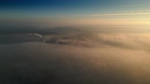 Smokestack Emitting Smoke Above Foggy City at Sunrise
