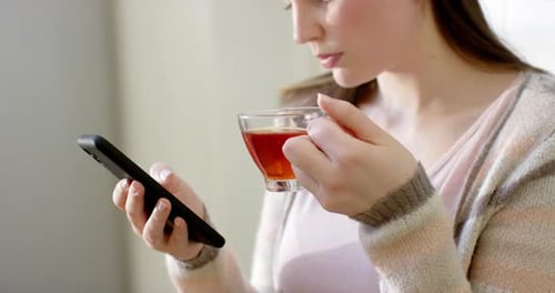 Woman Using Phone While Drinking Tea Indoors