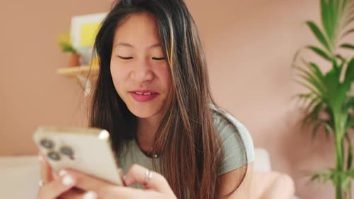 Close-up, smiling young woman sitting on the sofa writes SMS with a mobile phone