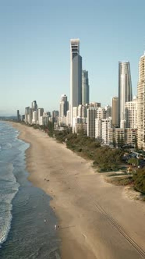 Vertical drone beach stretching far morning walkers sand waves crashing Gold Coast Queensland walk