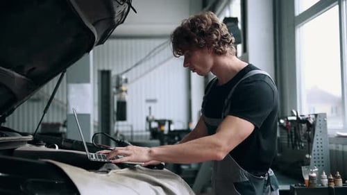 Computer diagnostics of cars, young mechanic specialist male uses laptop technology while repairing