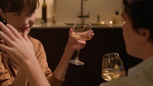 Frau spricht mit ihrem Freund, der ihre Hand hält, wenn sie während des Abendessens Wein trinkt