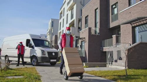 Caucasian Delivery Man in Face Mask and Gloves Carring Parcel Boxes on the Trolley Courier on the