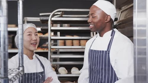 Portrait of happy diverse bakers in bakery kitchen with arms crossed in slow motion