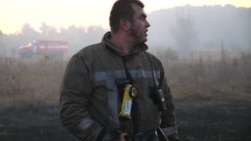 Tired Firefighter Standing Near Rural Field Fire