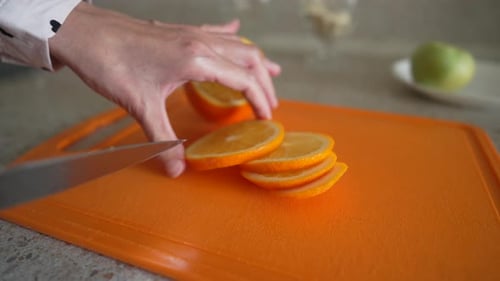 Woman slices orange on orange cutting board close-up
