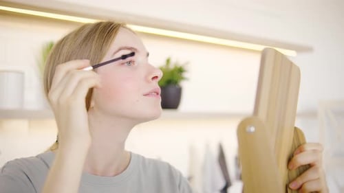A Young Woman is Applying Mascara While Standing in Front of a Stylish and Elegant Mirror Focusing
