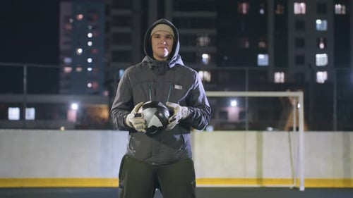 Thoughtful Man Holding Soccer Ball on Urban Sports Field at Night