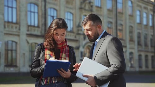 Bearded teacher and female student in discussion together in front of college
