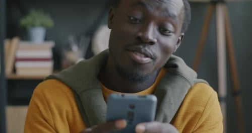 Joyful African American Man Using Smartphone Surfing Internet and Smiling Indoors in Office