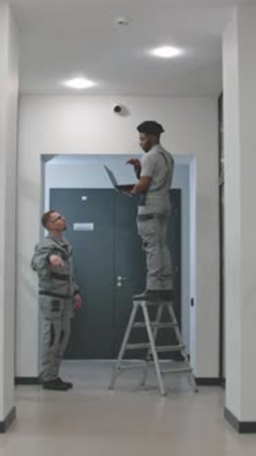 Multi Ethnic Installers in Uniform Sets Up Security Cameras in Office Corridor