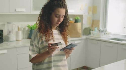 Woman Uses Credit Card with Mobile Phone in Kitchen