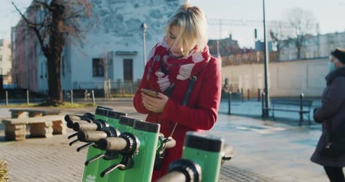 Woman Rents an Electric Scooter in a Parking Lot in the City
