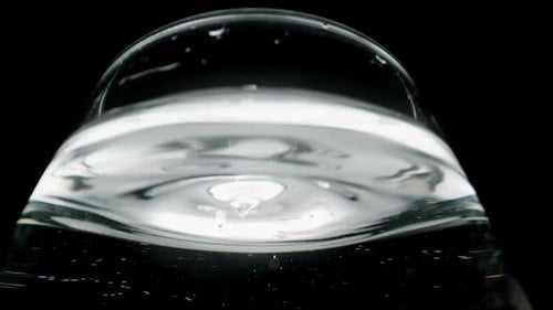 Water droplets dripping into the glass, macro view from a low angle on the silvery surface.