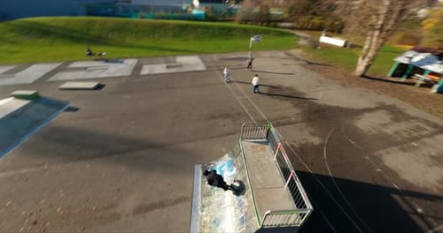 Dynamic FPV shot of Jake the BMXer in skatepark doing tricks on sunny autumn afternoon.